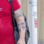 Фото тату: Крупный план татуировки на руке мужчины, изображающей сложный рисунок с элементами природы и мифологии. Уличная фотография, демонстрирующая детализацию рисунка.