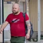 Фото мужчины с татуировками: абстрактный рисунок на руке, изображение головы животного на груди. Уличная фотография, демонстрирующая татуировки на теле.