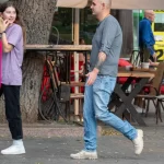 Фотография мужчины с татуировкой на предплечье: изображение летящих птиц, выполненное в черном цвете. Уличная съемка, демонстрирующая тату в повседневной жизни.