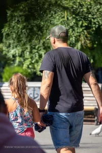 Фотография мужчины с татуировкой птицы на руке, идущего с маленькой девочкой. Тату выполнено в черном цвете, с акцентом на детализацию оперения.