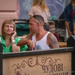 Крупный план руки мужчины с яркой татуировкой, сидящего в уличном кафе. Видны детали рисунка и окружающая обстановка.