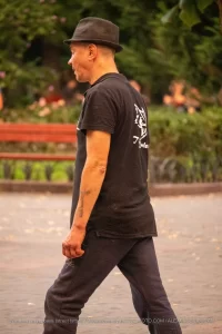Фотография мужчины в кепке и темной одежде с татуировкой волка на руке, идущего по улице.