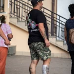 Фото тату на руке и ноге мужчины, идущего по улице. Детализированные рисунки в стиле реализм и традиционный, привлекающие внимание.