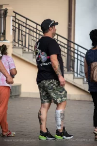 Фото тату на руке и ноге мужчины, идущего по улице. Детализированные рисунки в стиле реализм и традиционный, привлекающие внимание.
