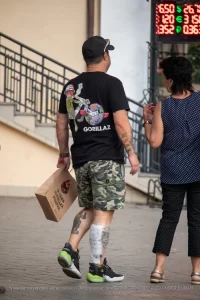 Фото тату на руке и ноге мужчины, идущего по улице. Детализированные рисунки в стиле реализм и традиционный, привлекающие внимание.