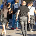 Фотография мужчины с полным рукавом татуировок, идущего по улице в окружении людей.