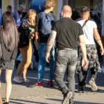 Фотография мужчины с полным рукавом татуировок, идущего по улице в окружении людей.