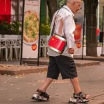 Фотография пожилого уличного музыканта с татуировкой на стопе, играющего на барабане с китайской символикой на фоне осеннего города.