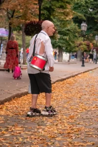 Фотография уличного музыканта с красным барабаном и рваной рубашкой, идущего по осенней аллее. Необычный пример использования тела как холста для тату.