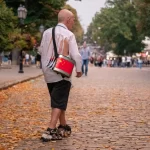 Фотография уличного музыканта с красным барабаном и рваной рубашкой, идущего по осенней аллее. Необычный пример использования тела как холста для тату.