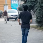 Фотография мужчины, едущего на электросамокате, с видимой татуировкой на руке. Городской пейзаж и динамичная поза.