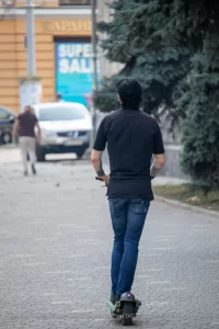 Фотография мужчины, едущего на электросамокате, с видимой татуировкой на руке. Городской пейзаж и динамичная поза.