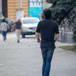 Фотография мужчины, едущего на электросамокате, с видимой татуировкой на руке. Городской пейзаж и динамичная поза.