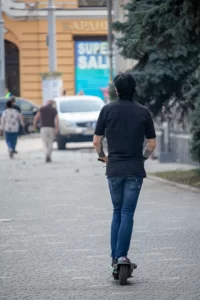 Фотография мужчины, едущего на электросамокате, с видимой татуировкой на руке. Городской пейзаж и динамичная поза.