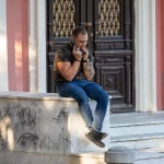 Фотография мужчины с татуировкой на руке, сидящего на ступеньках здания. Видна часть татуировки на плече.