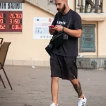 Фотография мужчины с татуировкой на икре, разговаривающего по телефону на улице. Татуировка выполнена в ярком стиле с использованием красного и черного цветов.