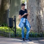 Фото татуировки на руке мужчины, использующего смартфон. Виден современный стиль одежды и детализированный рисунок на коже.