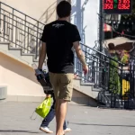 Фото тату на руке и спине мужчины: рукав с рисунком, татуировки на лопатках, выполненные в темных тонах. Мужчина идет по улице.