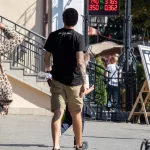 Фото тату на руке и спине мужчины: рукав с рисунком, татуировки на лопатках, выполненные в темных тонах. Мужчина идет по улице.