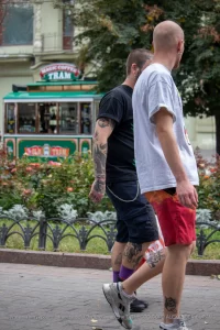 Фото мужчины с татуировками на руке и ноге на фоне старинного трамвая. Идеи для тату, эскиз тату, мастер тату.