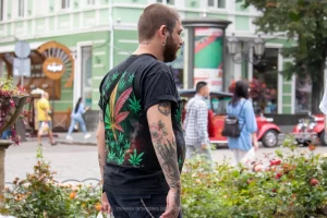 Фото татуировки на спине мужчины: листья марихуаны, черепа и другие элементы. Уличная фотография.