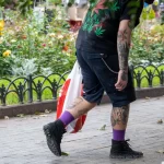 Фото татуировки на руке и ноге мужчины: рукав с черепами, листьями марихуаны и другими элементами. Уличная фотография.