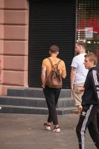 Фото мужчины с татуировками на руках, идущего по улице с рюкзаком. Видны фрагменты рисунков с цветами и абстрактными элементами.