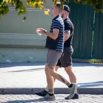 Фото тату на руке мужчины, выполненное в стиле олдскул. Изображены розы и надпись, выполненные черными чернилами. Уличная фотография.