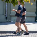 Фотография мужчины с татуировкой на ноге, идущего по улице. На заднем плане виден городской пейзаж.