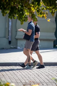 Фотография мужчины с татуировкой на ноге, идущего по улице. На заднем плане виден городской пейзаж.