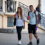 Фотография мужчины с татуировкой на руке, идущего по улице с женщиной. На заднем плане виден памятник и лестница.