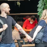 Фото тату на руке мужчины, идущего по улице с рюкзаком. Рисунок татуировки выполнен в стиле традиционной японской татуировки.
