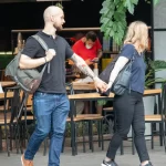 Фото тату на руке мужчины в стиле олдскул: корабль, роза, якорь, морские волны. Девушка держит мужчину за руку. Красочный рисунок татуировки.