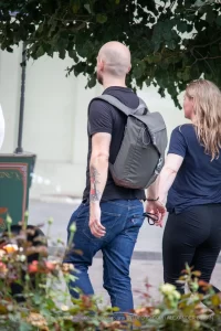 Фото тату на руке мужчины с рюкзаком, идущего по улице. Рисунок татуировки выполнен в ярких цветах и изображает мифологических существ.