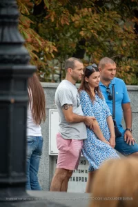 Фото мужчины с татуировкой спирали на руке, стоящего рядом с женщиной и другим мужчиной. Татуировка выполнена в черном цвете.