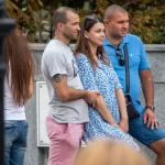 Фото мужчины с татуировкой на руке, стоящего рядом с женщиной и другим мужчиной. Татуировка представляет собой спираль.