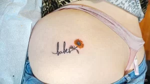 Фото тату: надпись 'babes' и маленький подсолнух на женском боку. Нежный и стильный рисунок татуировки в черных тонах.