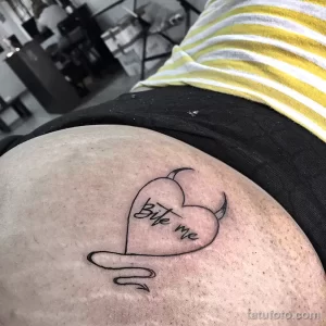 Фото тату: Надпись 'Bite me' внутри сердца с рожками, выполненная на коже. Игривый и провокационный дизайн.