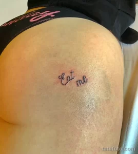 Фото тату: надпись 'Eat me' выполнена простым шрифтом на женском бедре. Минималистичный рисунок татуировки, вызывающий и игривый.
