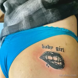 Фото татуировки на боку с изображением женских губ с клыками и надписью 'baby girl'. Рисунок выполнен в черном цвете с добавлением капель крови.