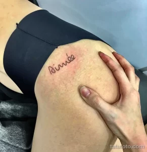 Фото татуировки с надписью 'Aimée' на плече. Простой и элегантный дизайн, выполненный черными чернилами.