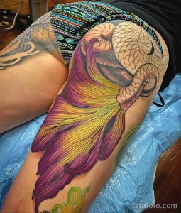Фото тату яркой рыбы-бабочки, выполненной в акварельной технике на бедре. Рисунок татуировки с плавными переходами цветов и детализированными плавниками.