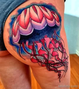 Фото татуировки на бедре с изображением медузы, выполненной в ярких цветах и стилизованной под витраж.