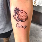 Фото татуировки ежика с надписью 'Grizzy' на руке. Нежный и милый рисунок татуировки в черном цвете.
