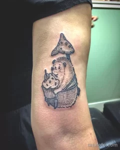 Фото татуировки ежа, спрятавшегося под шляпкой гриба, в технике blackwork. Контурный рисунок, детализированная проработка, сказочный сюжет. Идеально для любителей природы и фэнтези.