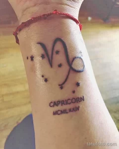 Фото татуировки Козерога с символом знака зодиака, надписью "CAPRICORN" и датой рождения в римских цифрах. Персонализированный и значимый рисунок татуировки.