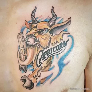 Фото яркой татуировки с изображением головы козла и надписью "Capricorn". Цветная татуировка на груди.