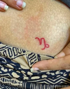 Фото минималистичной татуировки символа Козерога на коже. Красный цвет, простой дизайн, небольшие размеры.