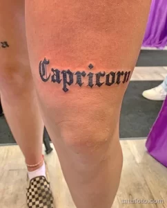 Фото минималистичной татуировки с надписью 'Capricorn' на бедре. Простой, но стильный дизайн в готическом стиле.