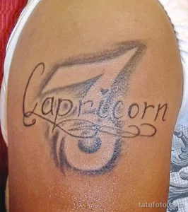 Фото татуировки Capricorn на плече, выполненной в серо-черных тонах с использованием тени и декоративных элементов.